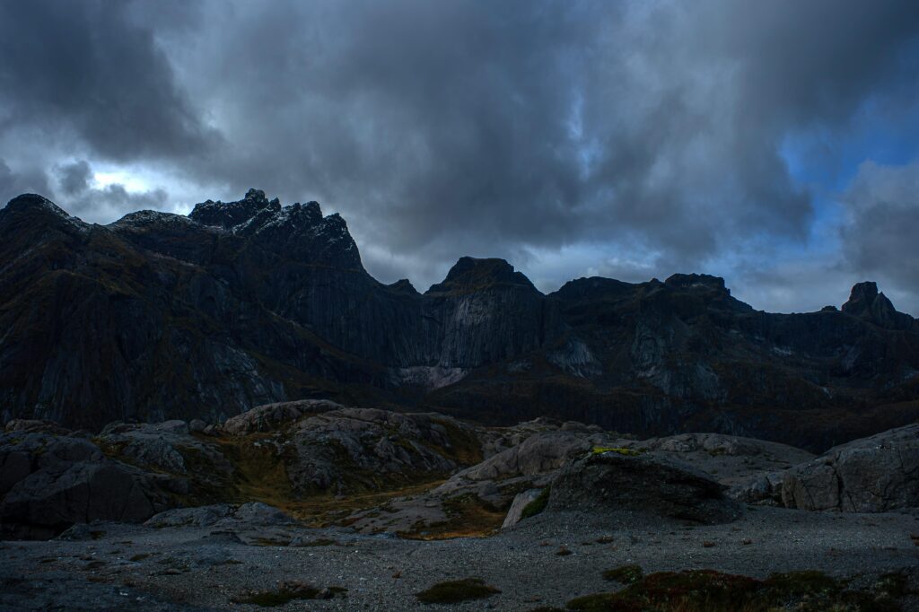 Twilight view of dramatic mountain peaks under cloudy sky in Nusfjord, Norway.