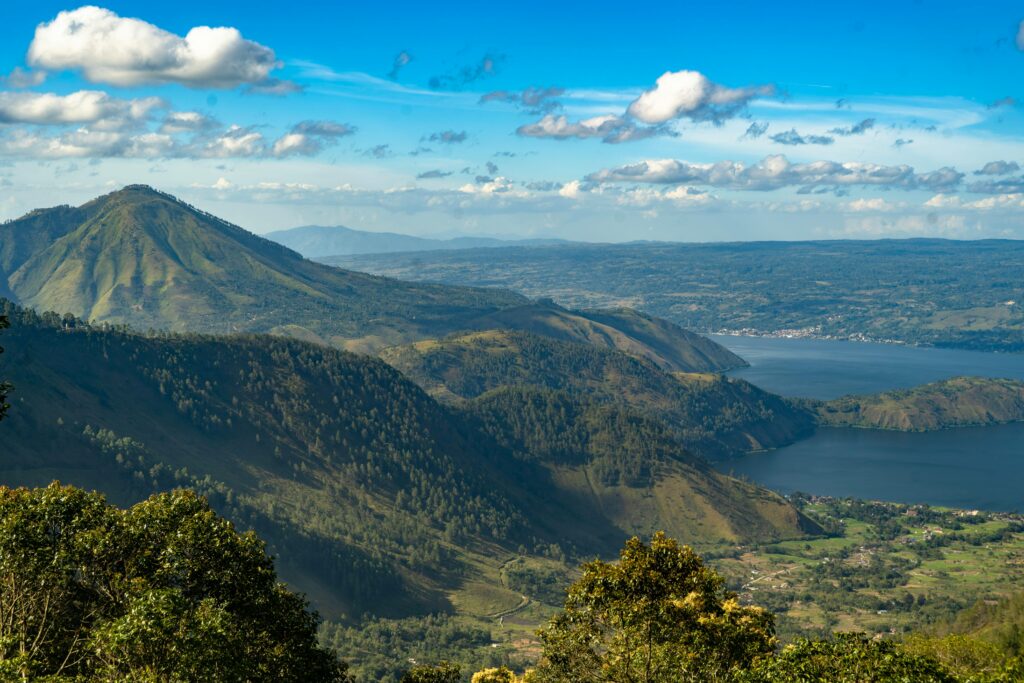 A breathtaking aerial view of Lake Toba in Sumatra, surrounded by lush mountain landscapes under a vibrant sky.